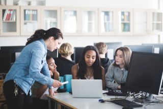 Teacher assisting female students using laptop in computer lab at high school