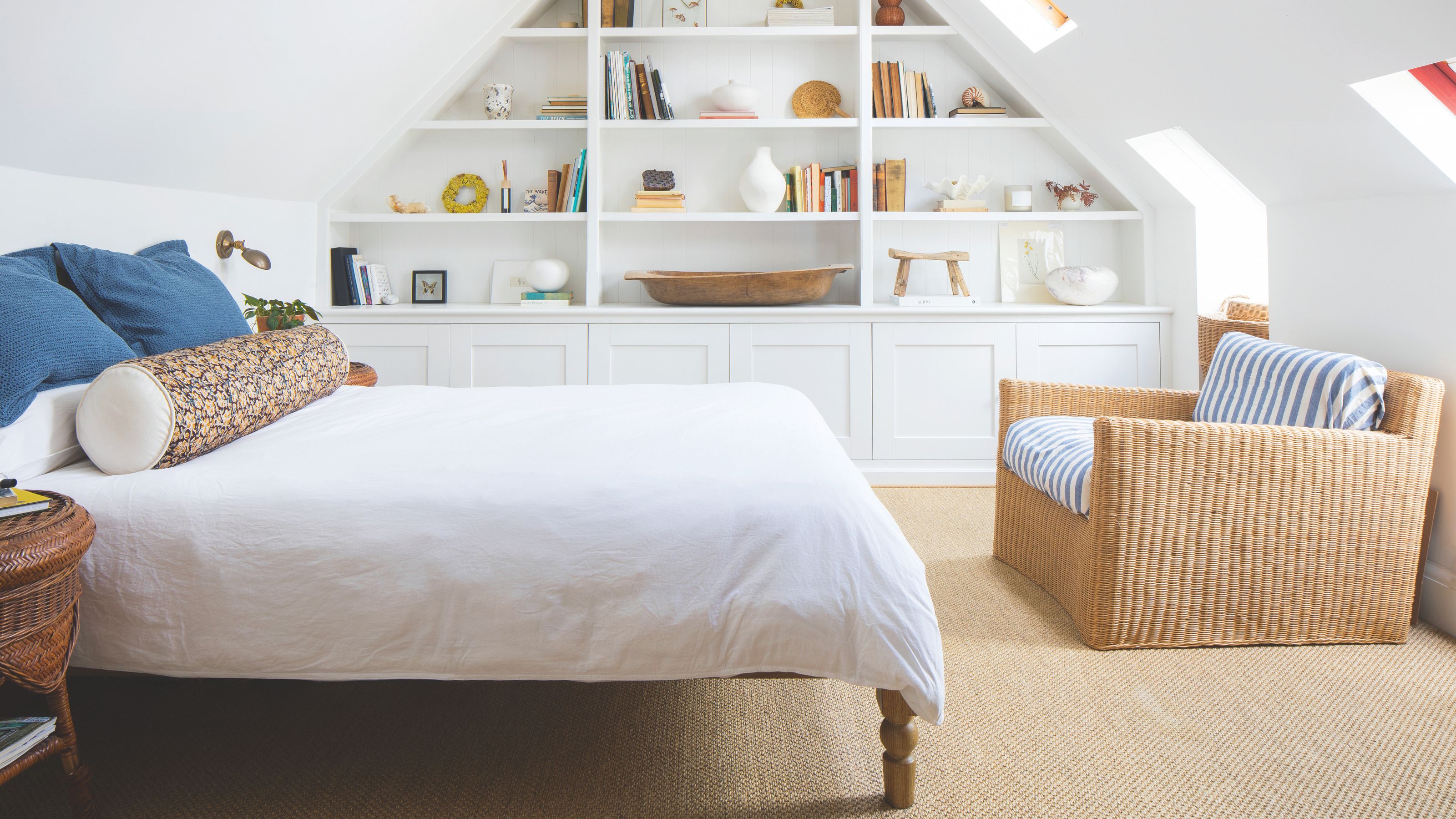 White painted loft bedroom with a white bed, cream carpet, a wicker snuggle chair and bookcases on the wall