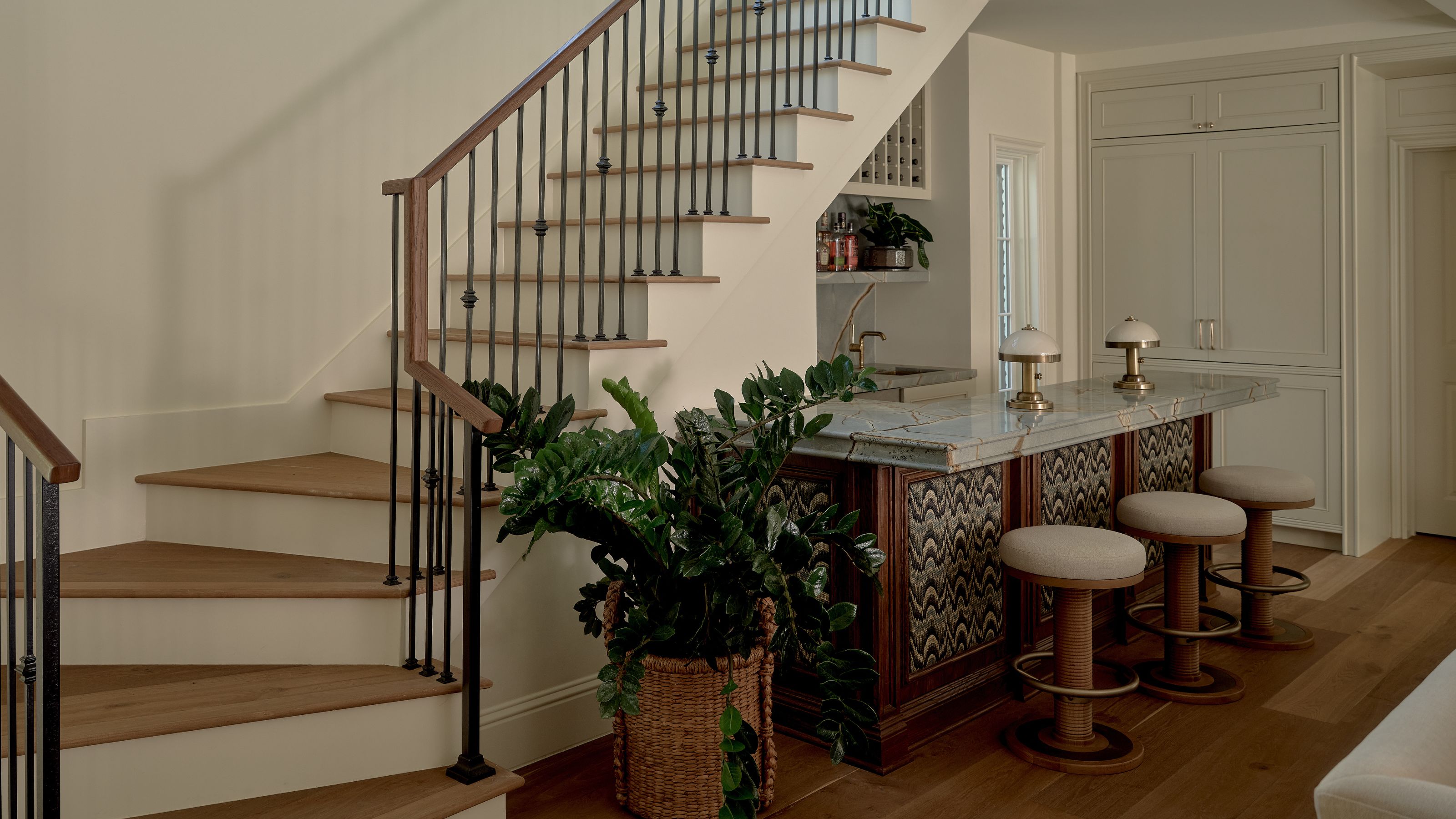 an open plan downstairs with a neutral wooden staircase with black railings and a home bar tucked beneath