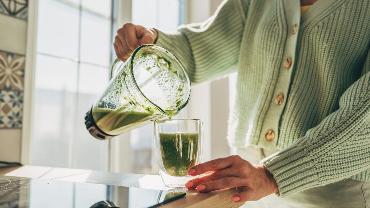 A woman making a green smoothie in her kitchen at home