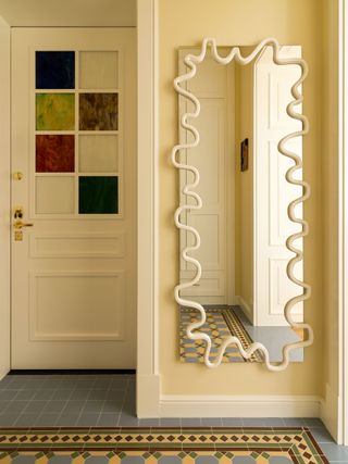 a pale yellow entryway with a wavy mirror