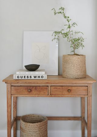 An entryway table with a set of books, a basket planter and a bowl