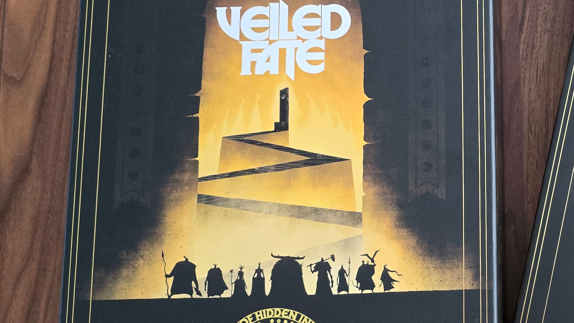 Veiled Fate box displaying the logo, a maze, and silhouettes heroes, sat on a wooden surface