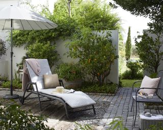 How to plan a small garden illustrated with a sun lounger and parasol in a paved garden, with a white wall and climbing plants.