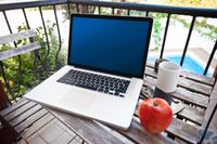 Laptop computer on the table in the terrace, pool in background.