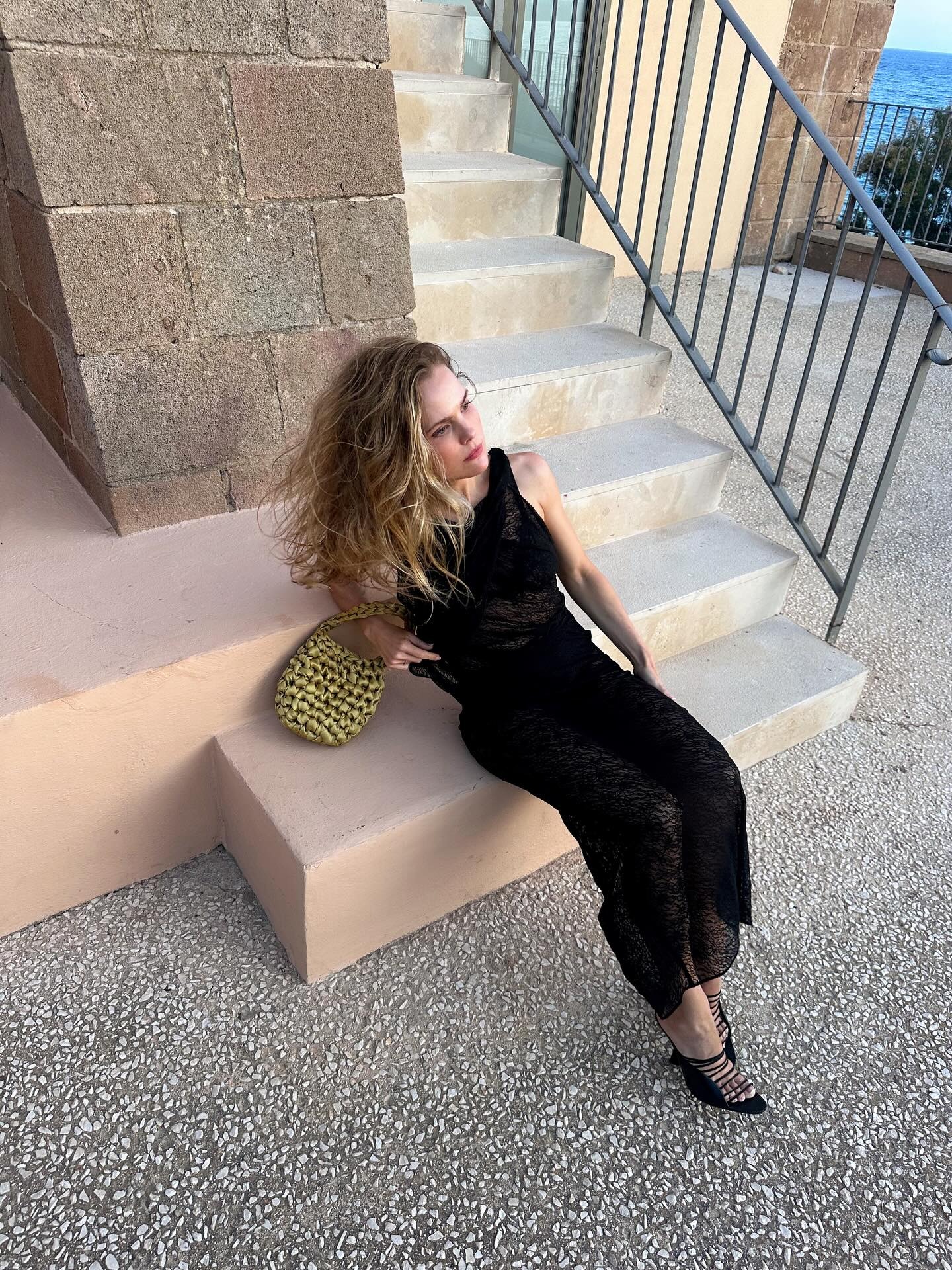 A woman with blonde hair posing at the base of a staircase.