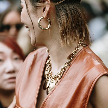 Woman wearing gold hoop earrings and gold chain tag necklace while attending Paris spring summer 2025 fashion week 