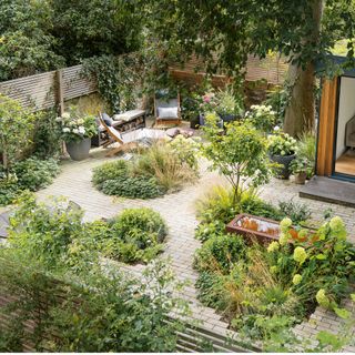 Birds eye view of the garden with a garden room, patio seating area, water feature and borders of green shrubs