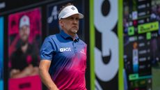 Ian Poulter in a pink and blue shirt with white visor walking