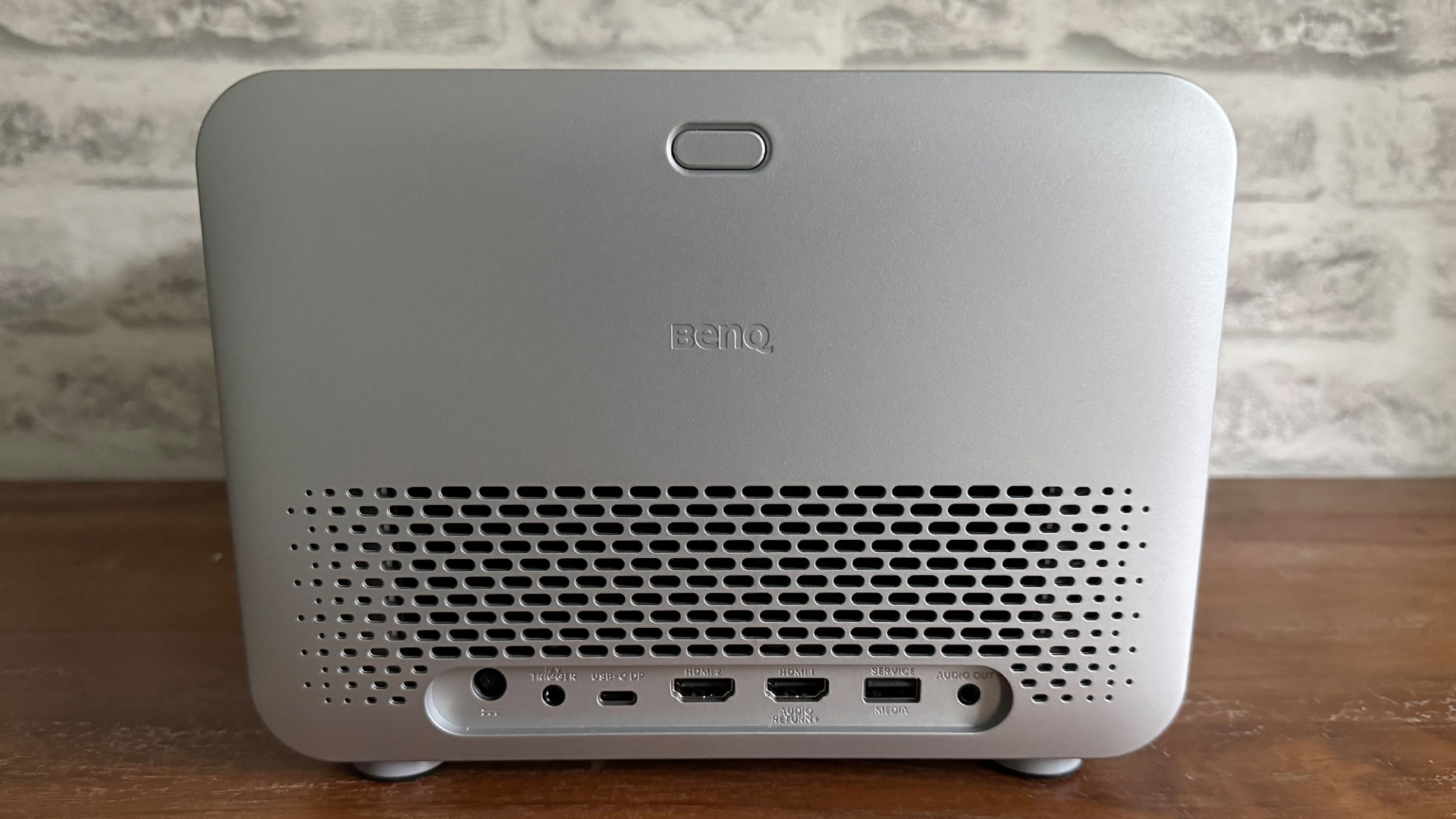 BenQ TK705i home cinema projector on wooden sideboard in front of white brick wall, rear of unit showing connections