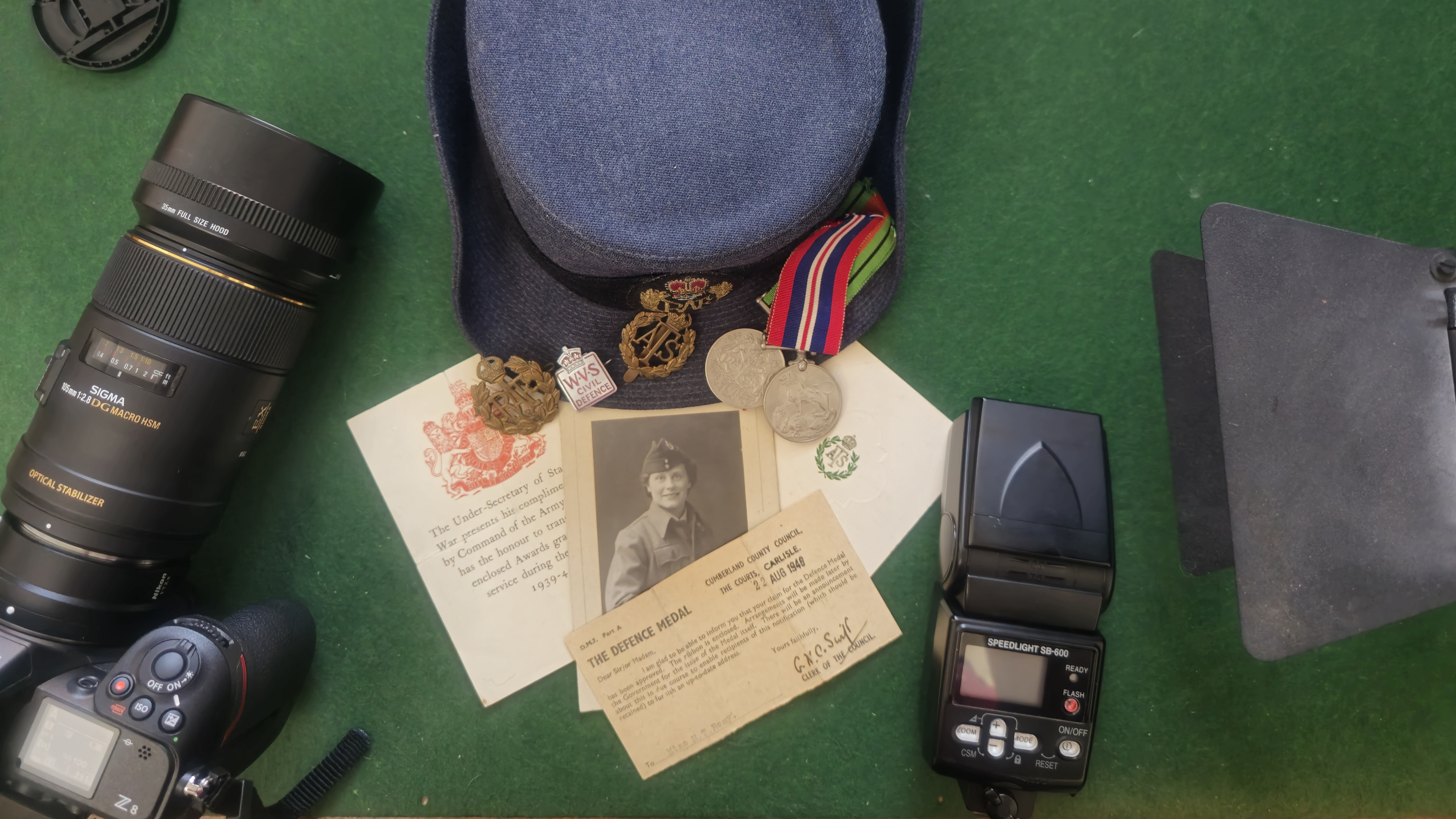 An arrangement of militaria, showing medals, cards and a cap, along with a Sigma 105mm macro lens and SB-600 flash