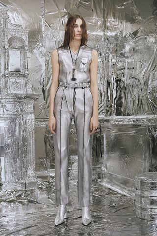 Model wears a silver denim jumpsuit surrounded by a foil room