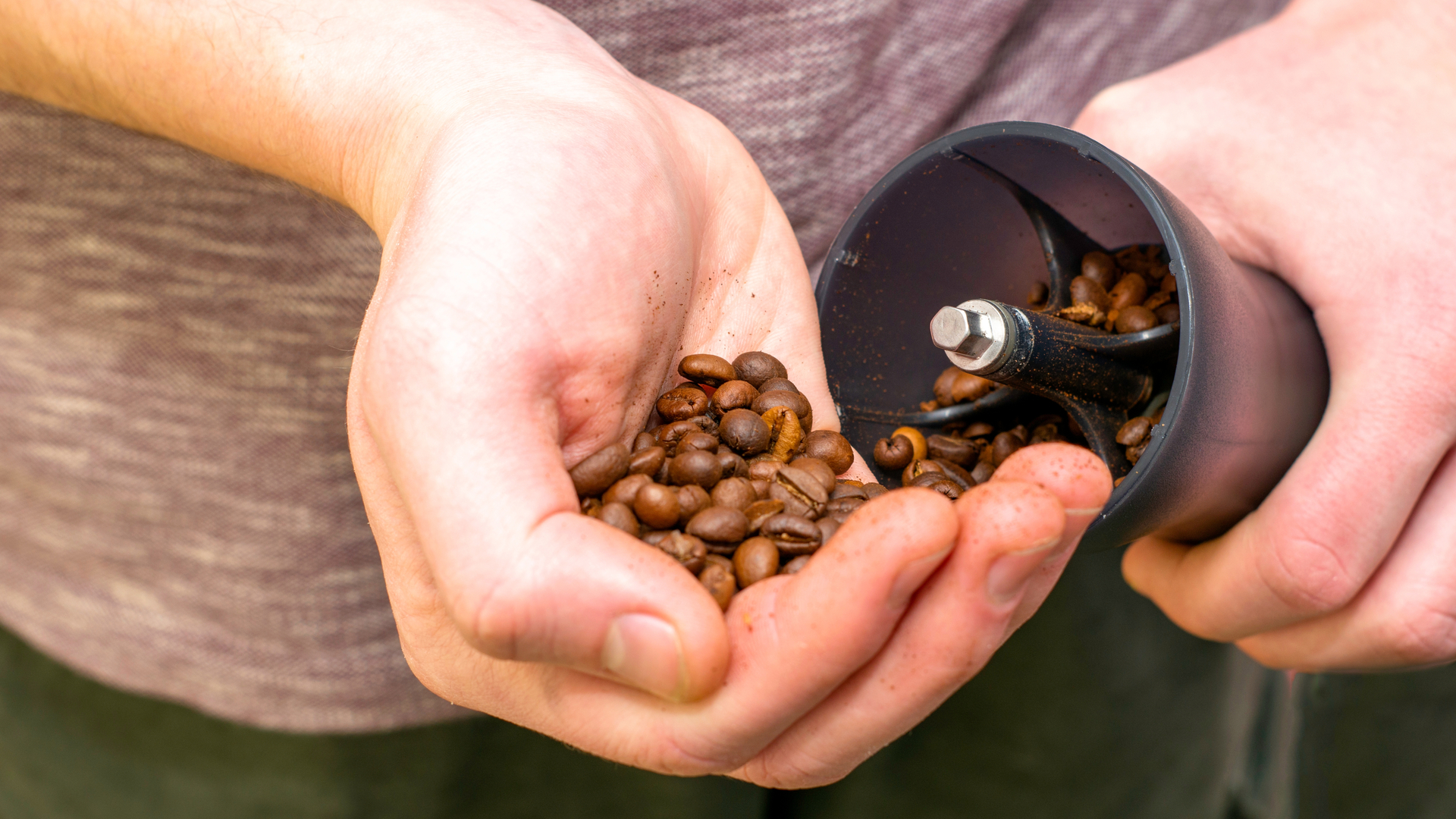 Coffee beans being poured by hand into a manual coffee grinder demonstrating how to make espresso
