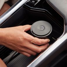 Woman's hand with gold ring holding Pura diffuser in car