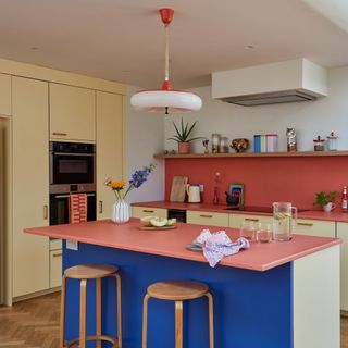 Blue island in kitchen with wooden bar stools and cream base units with pink work surface and splashbacks