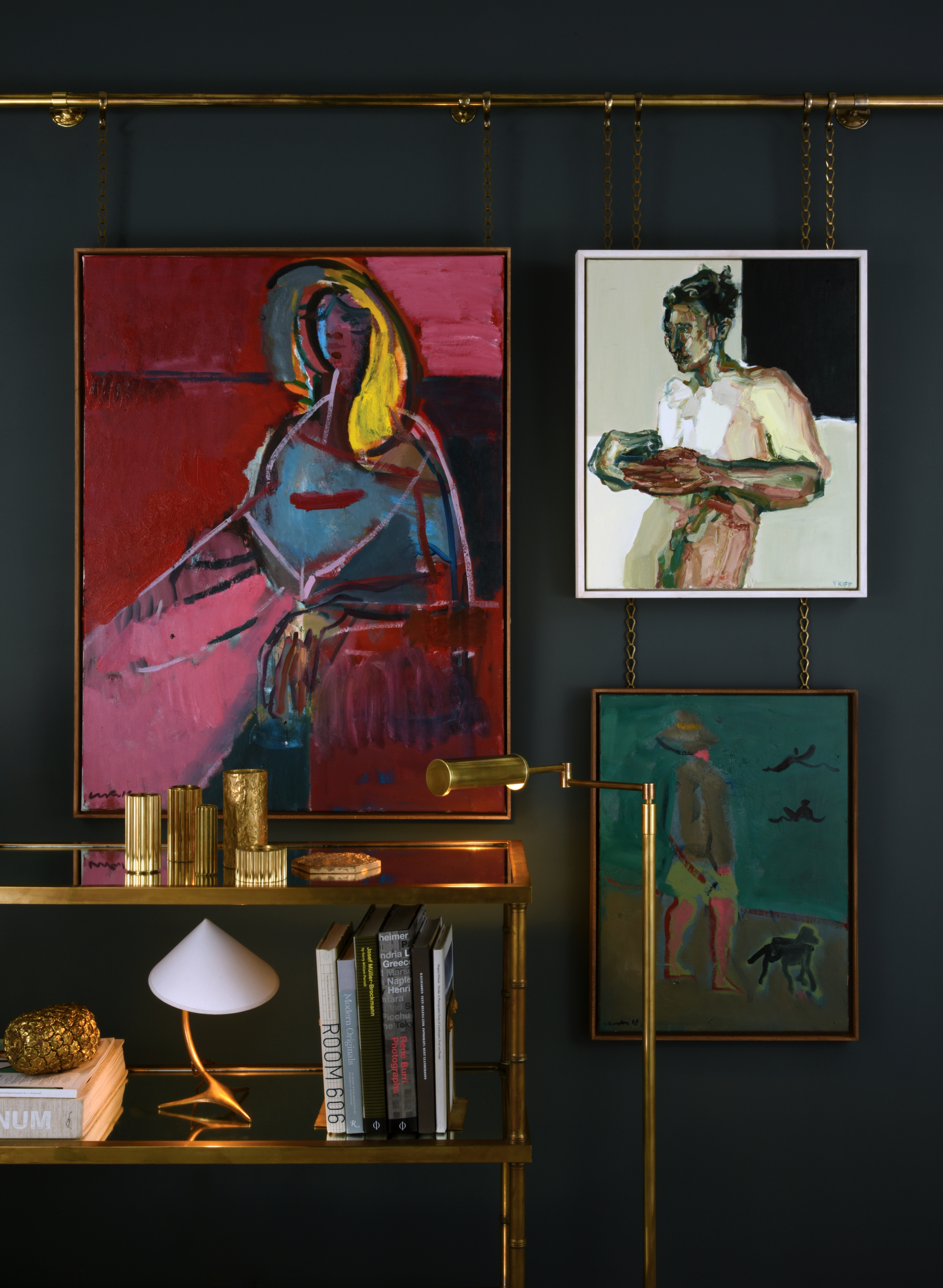 brass Collier Webb picture rail with three artwork hanging above a console styled with lamps, books, and dishes, and a brass, swing-arm floor lamp