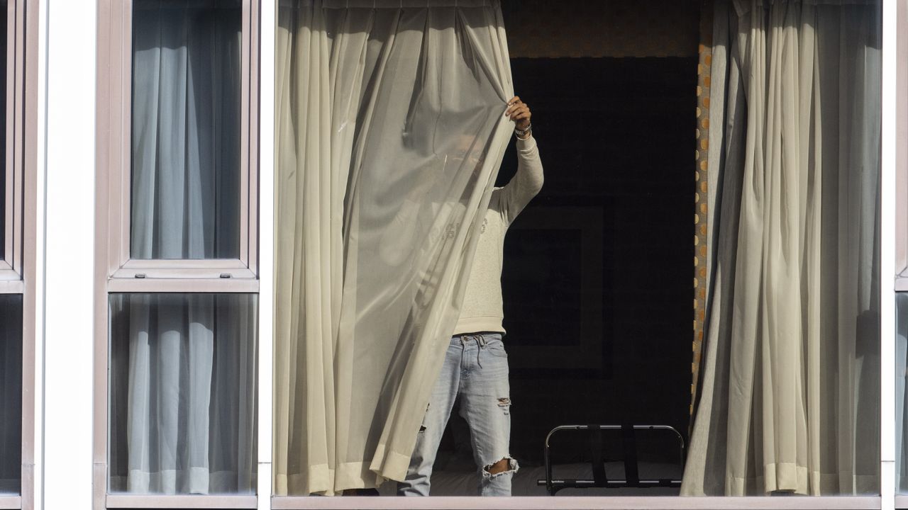 A man draws his curtains at the Radisson Blu hotel after arriving at Heathrow