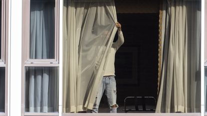 A man draws his curtains at the Radisson Blu hotel after arriving at Heathrow