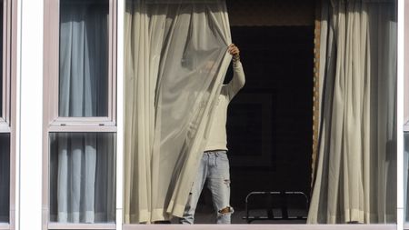 A man draws his curtains at the Radisson Blu hotel after arriving at Heathrow