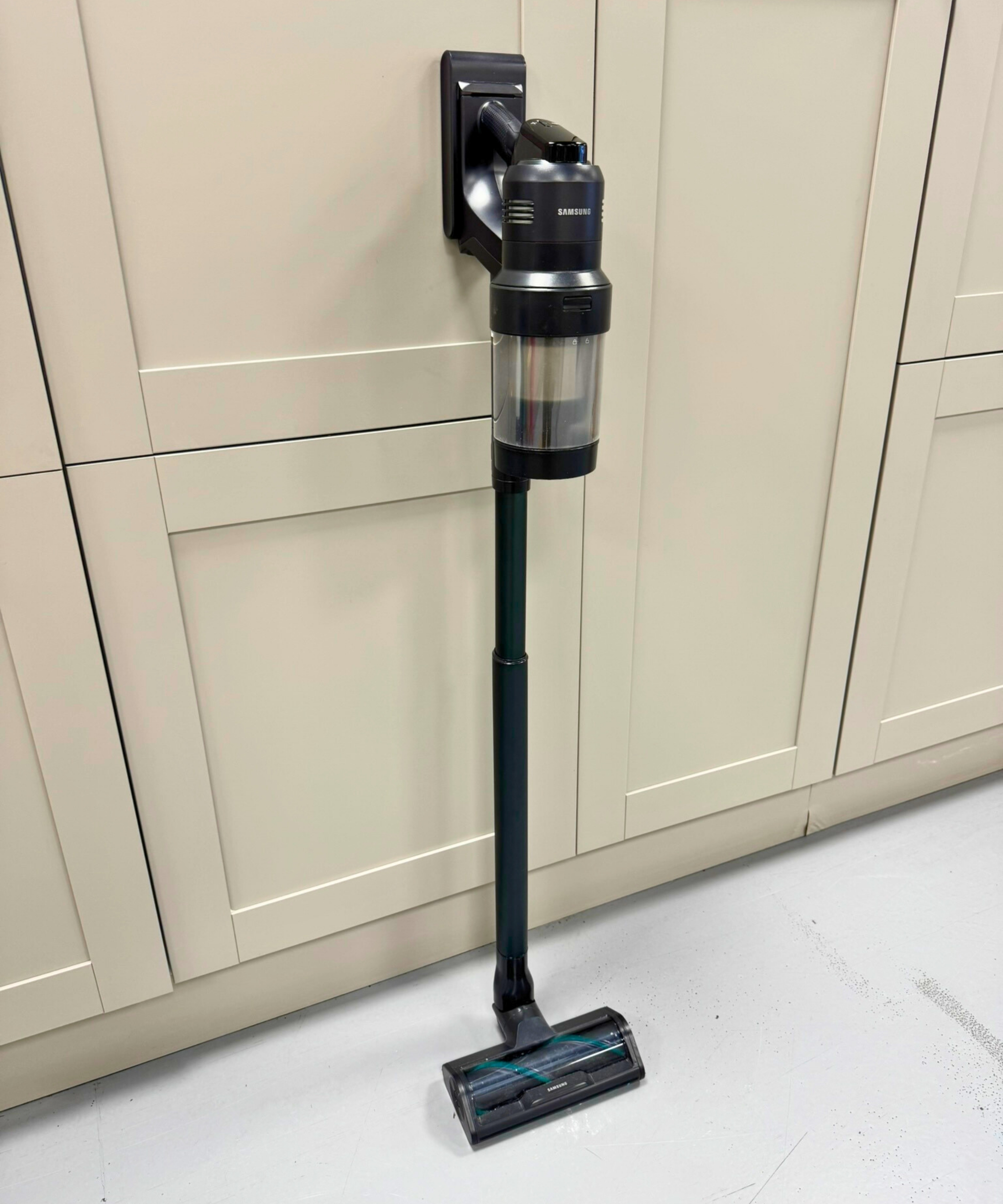 Samsung Bespoke AI Jet Ultra cordless vacuum leaning on cabinets on gray floor.