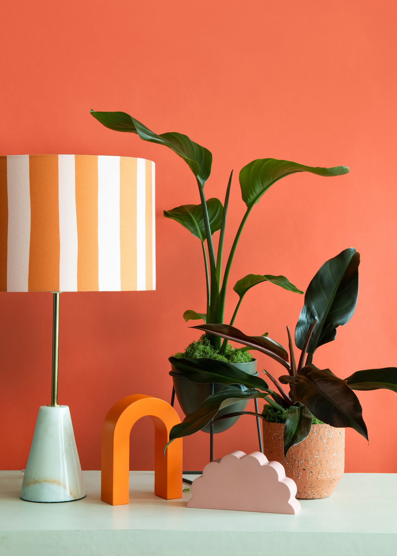 A mint green table with a set of potted houseplants in front of an orange wall