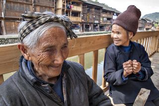 Older Chinese women rest on a bench in the middle of rural street in the countryside in Zhaoxing Dong Village, Guizhou Province, China.