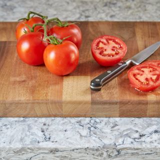 Tomatoes on wooden cutting board next to kitchen knife, marble kitchen worktop