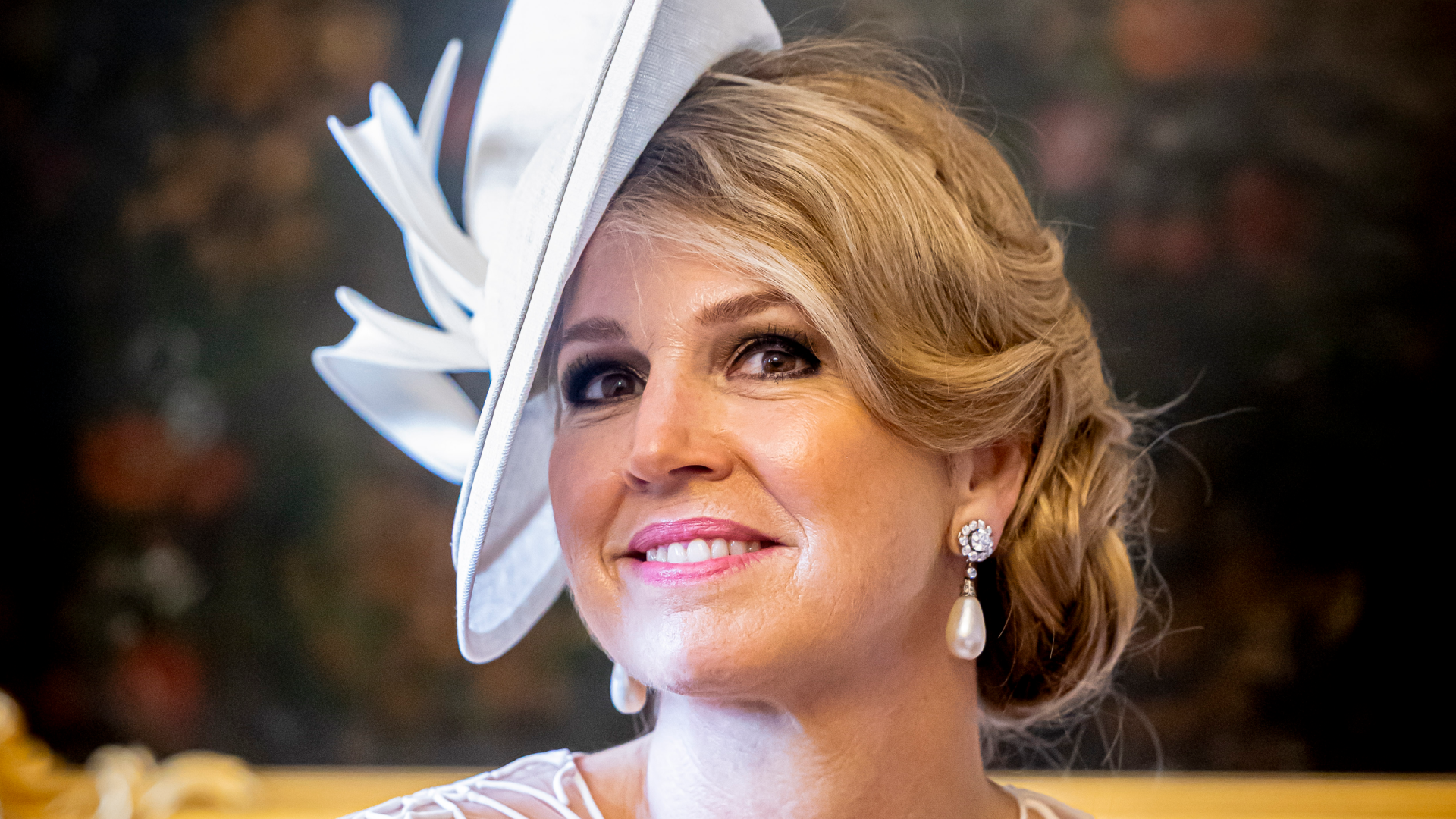 Queen Maxima wearing a white hat and lace dress with pearl earrings