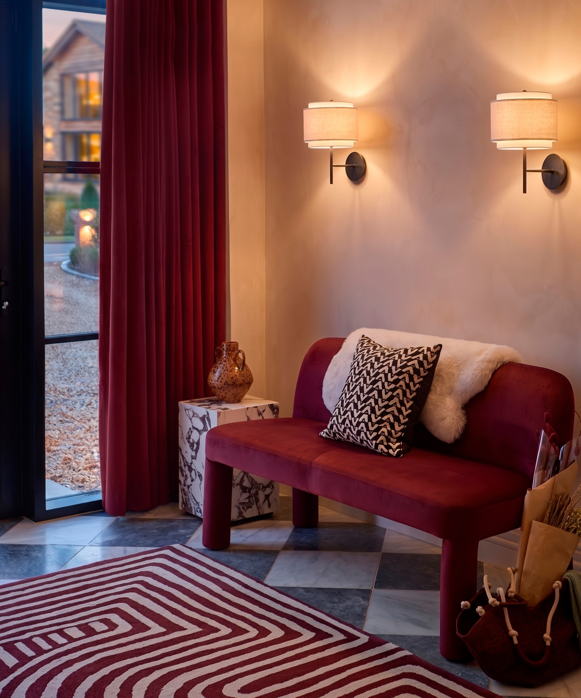 Burgundy velvet bench with striped rug and wall sconces beside open door with red curtain to garden.