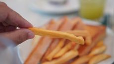 A close up of a bundle of yellow french fries with a left hand grasping one.