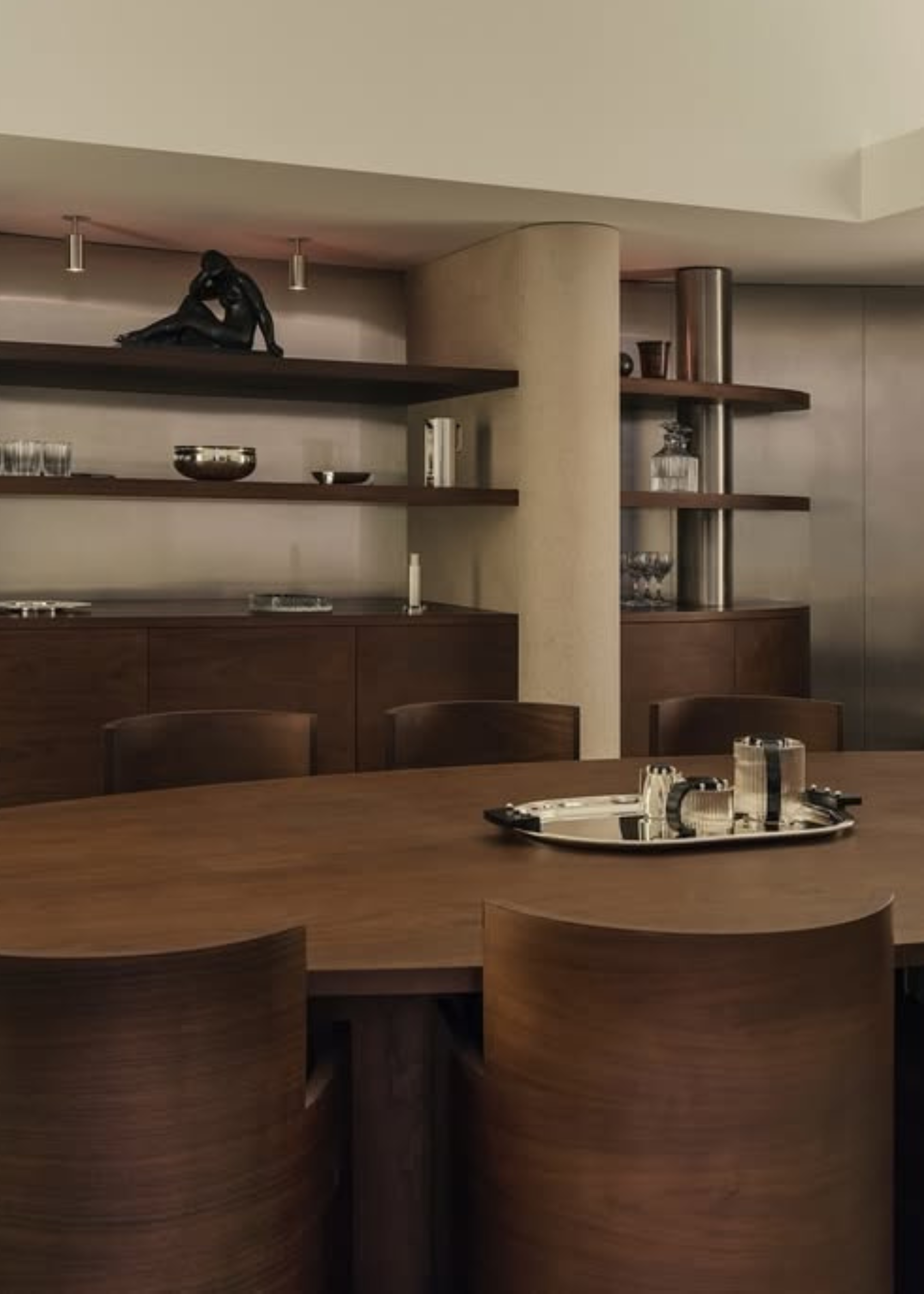 A minimalist living room with chrome walls, wood shelving, a wood dining set with a tray on the table, and muted beige walls