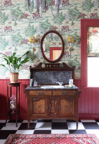 An antique wooden bathroom vanity in front of a red paneled wall in a bathroom with black and white floor tiles
