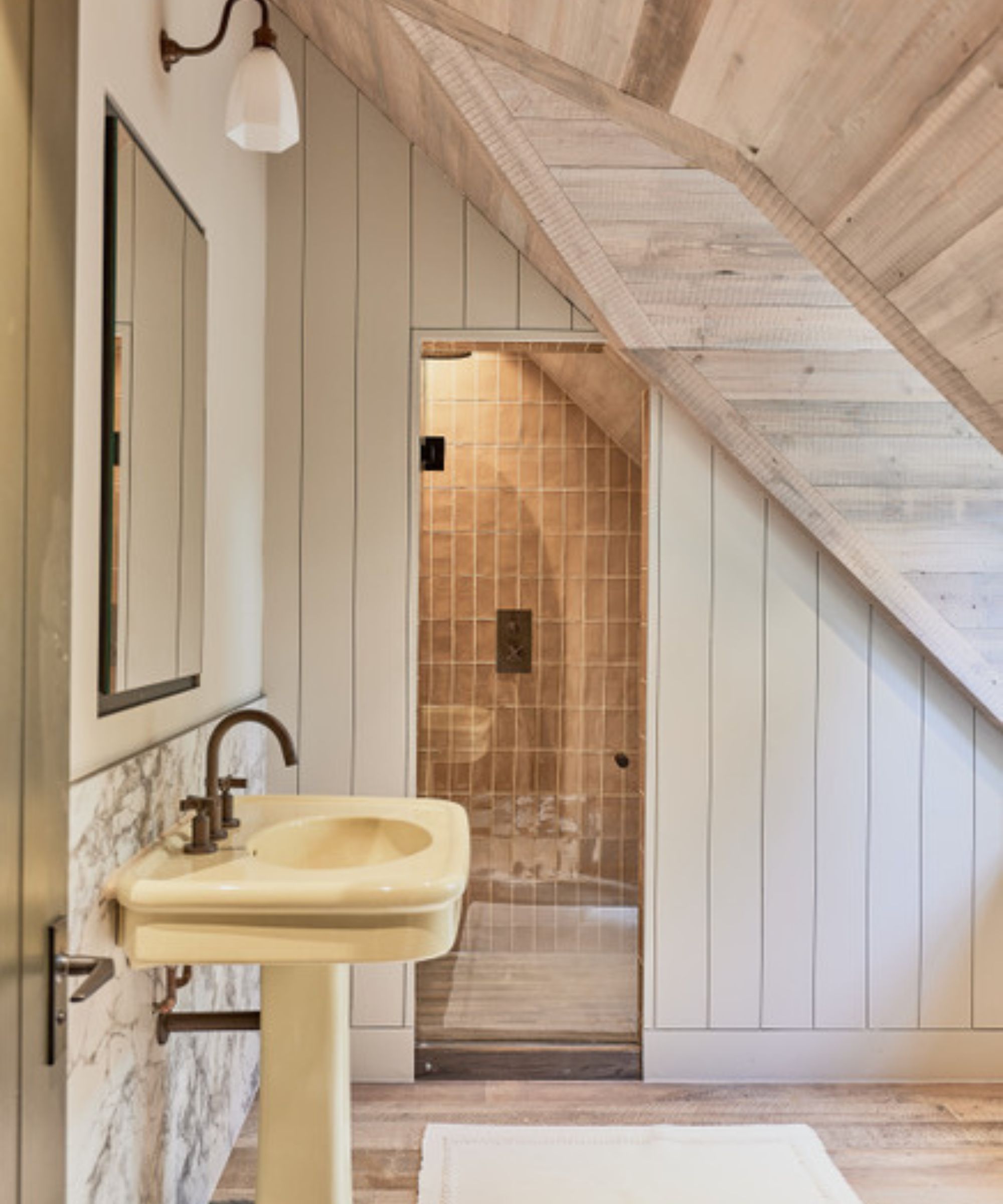 A loft conversion bathroom with a sloped, timber-clad ceiling, a wooden floor, marble splashback and shower