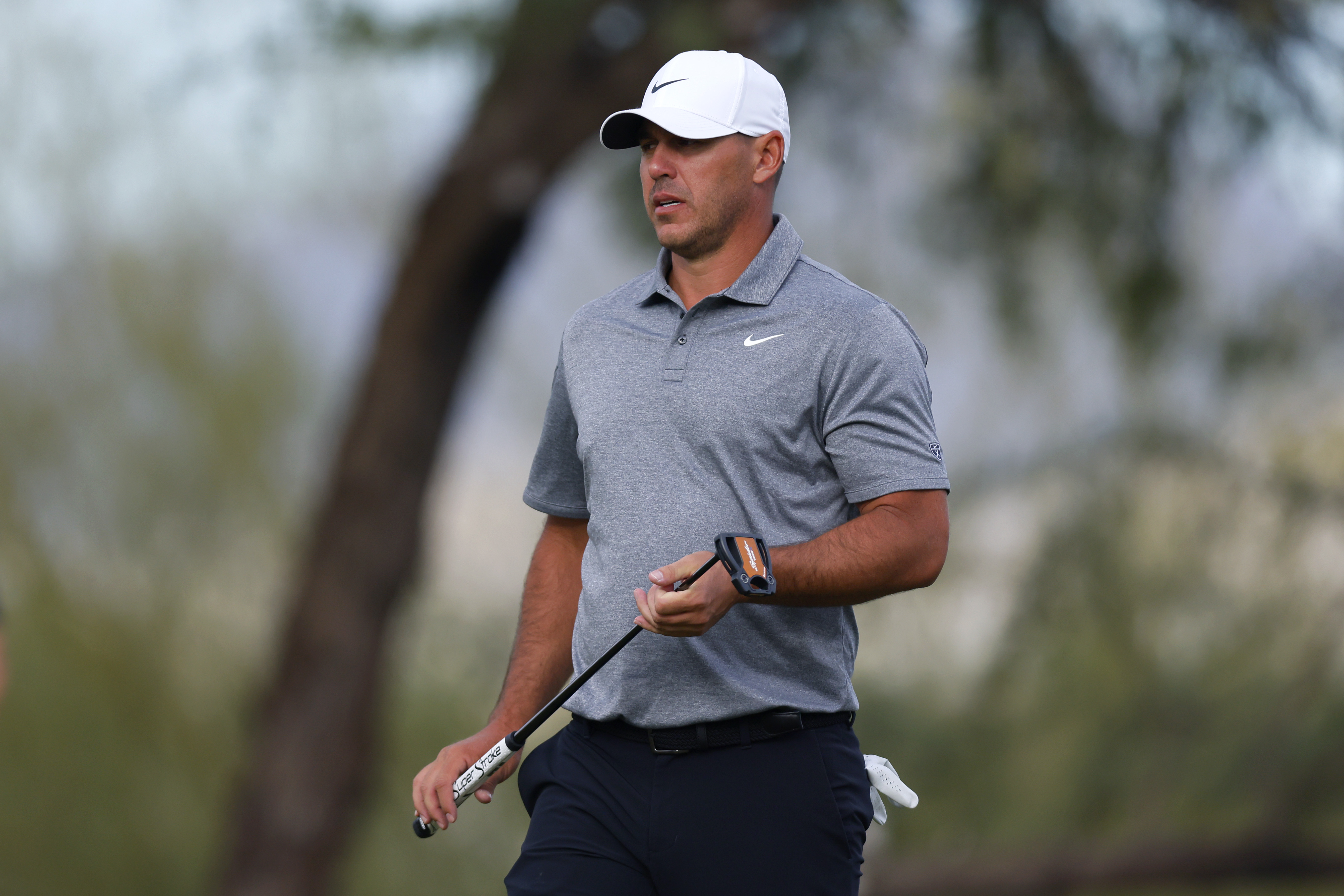 Brooks Koepka walks off the green holding a putter