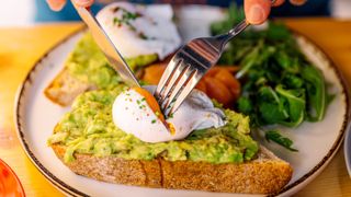 Person eating avocado toast with poached egg and salmon, close-up view