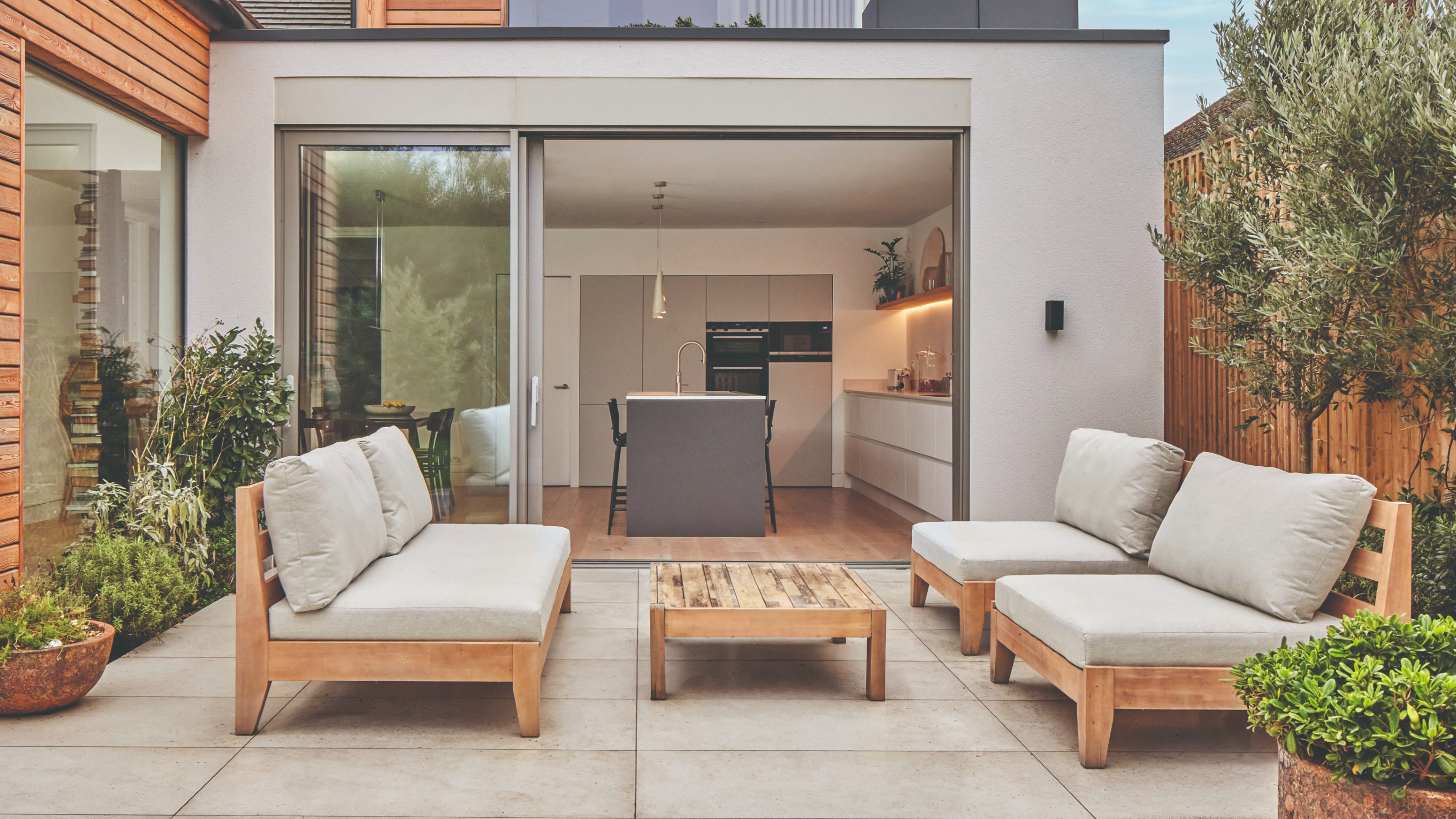 A patio with a slightly weathered wooden outdoor lounge set with off-white cushions 