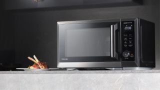The toshiba microwave on a surface with some food beside it