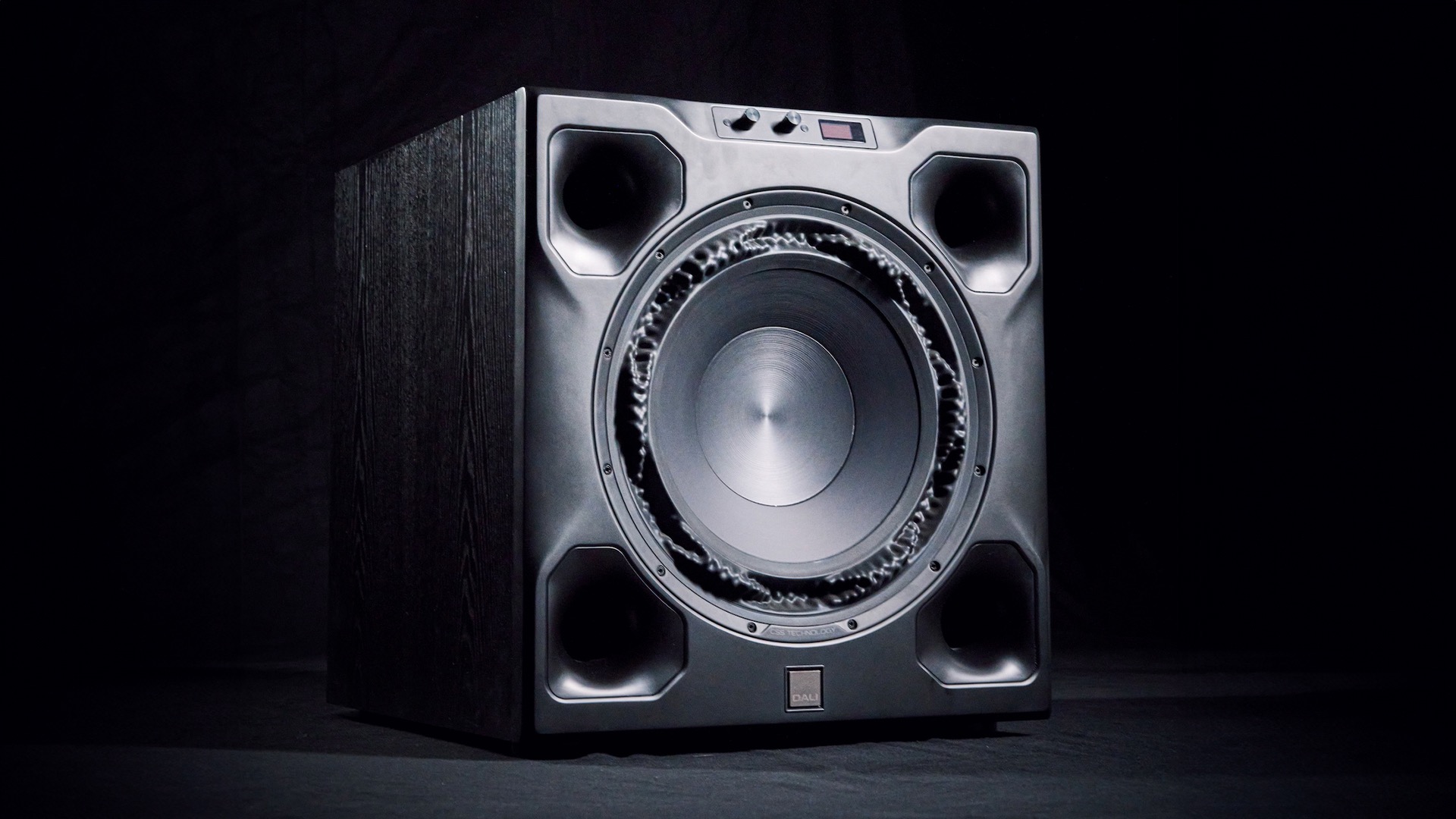 A black Dali V-16 F subwoofer on a black background.