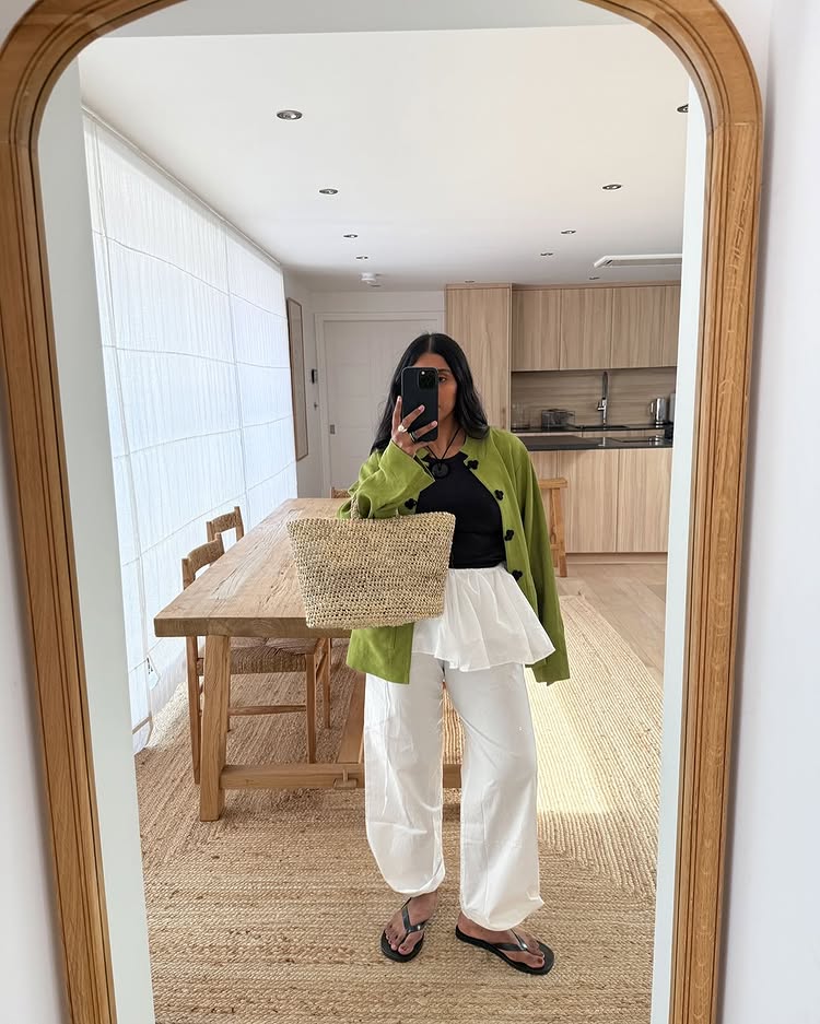 @monikh wears a pair of black flip flops with white linen trousers and a green knitted cardigan