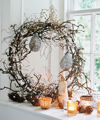 Christmas window decor ideas with a twig wreath and assorted candles on a white window sill