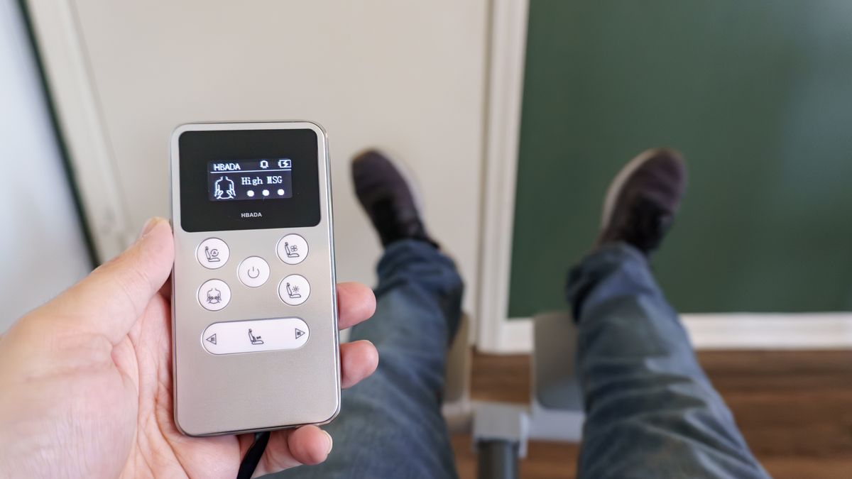 A person holding the remote for the Hbada X7 office chair while reclining in it with their feet up