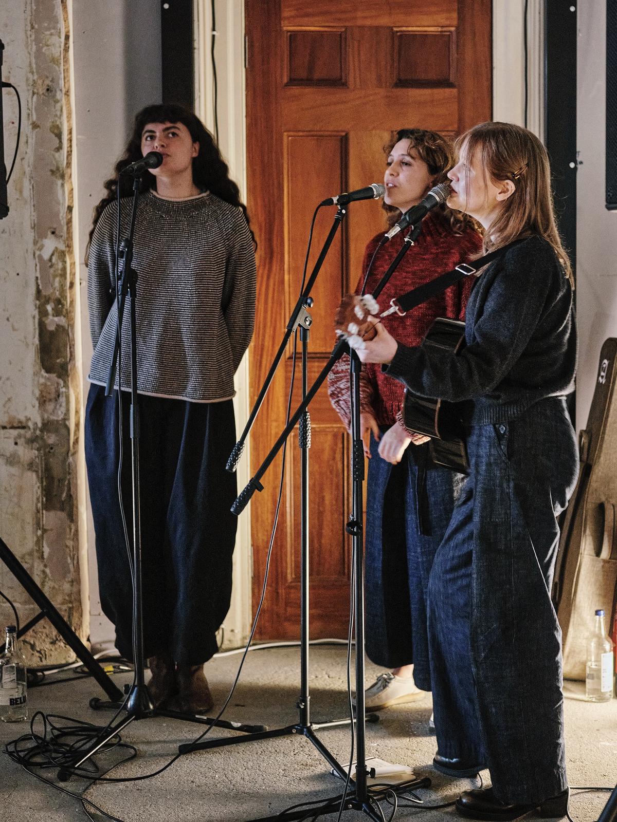 A series of installation shots from a show hosted inside a historical building with unfinished walls and tall ceilings captures the soft atmosphere inside it, punctuated by floating artworks, crafty furniture and accessories, and people chatting or performing.