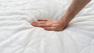 A man's hand resting on the surface of a soft memory foam mattress