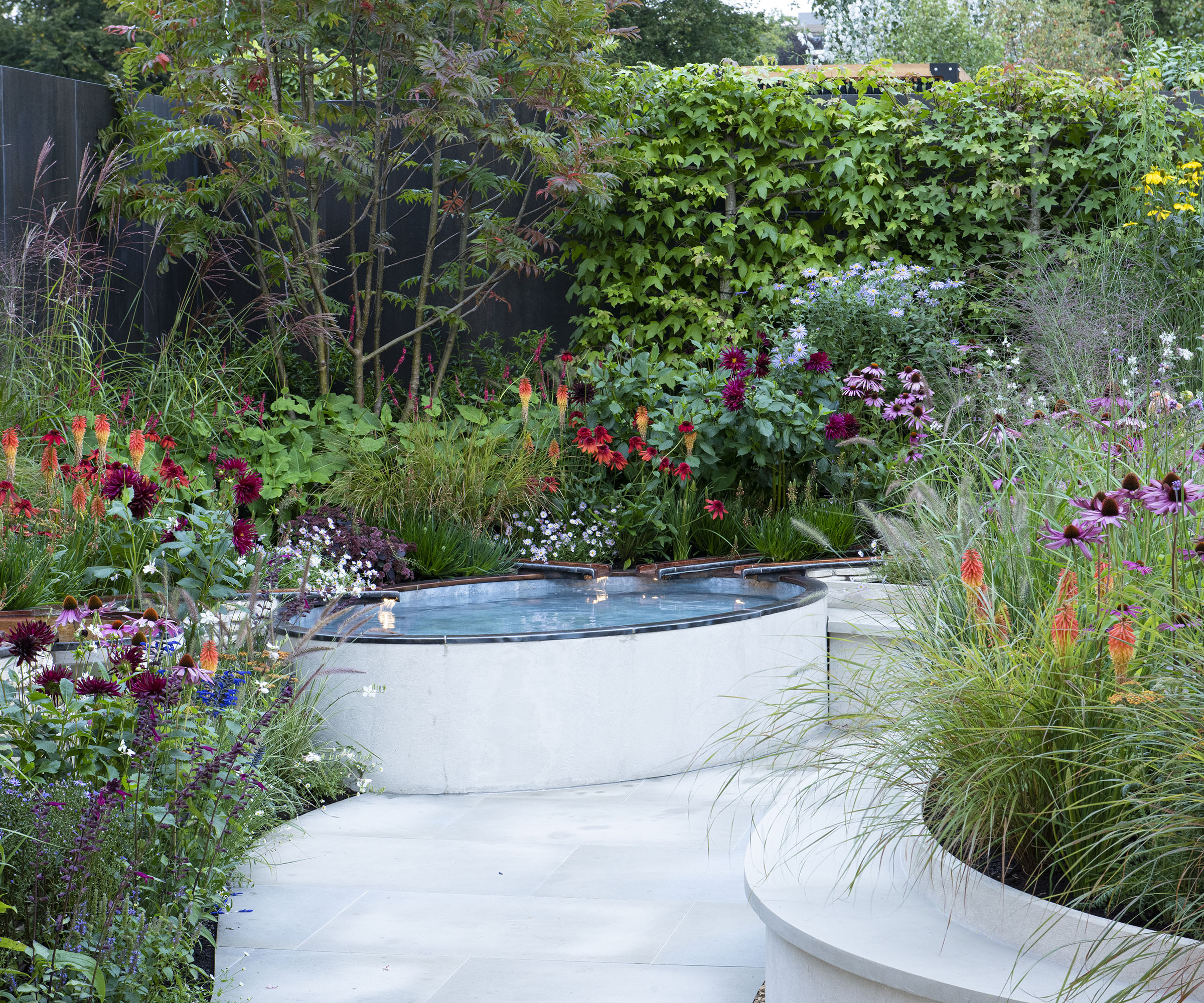 A curved garden with bright summer blooms and a sculptural water feature