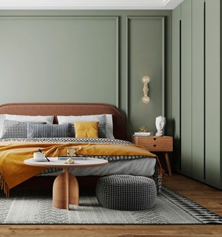 green bedroom with turmeric blanket and cushion, black and white bedding and rug, brown bed, wood side table and coffee table, wall light