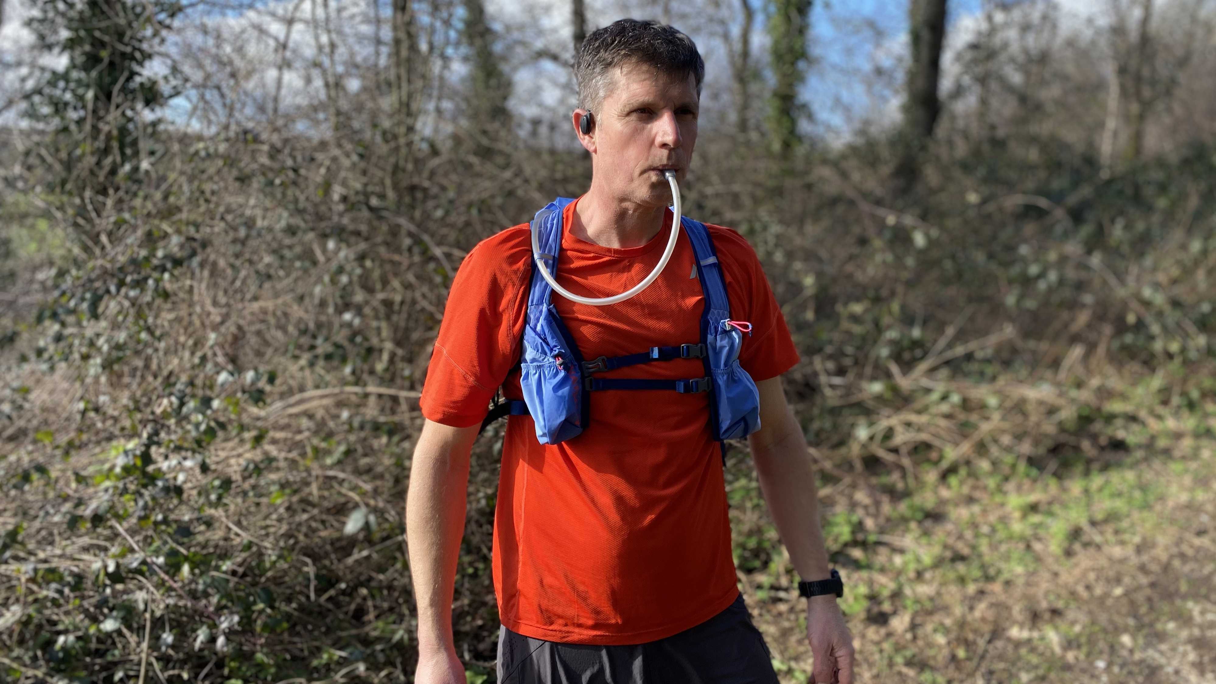 Runner drinking from the Nathan TrailMix 2.0 12L Hydration Pack in woodlands