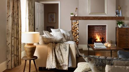 A cozy living room with a cream sofa filled with throw cushions, and a it fireplace with firewood stacked beside it