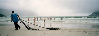 Ex-prisoner Marc cleaning Hout Bay Beach. He is wearing black and blue and there are multiple people in the sea