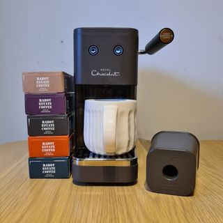 Hotel Chocolat Podster next to stack of boxes of coffee pods