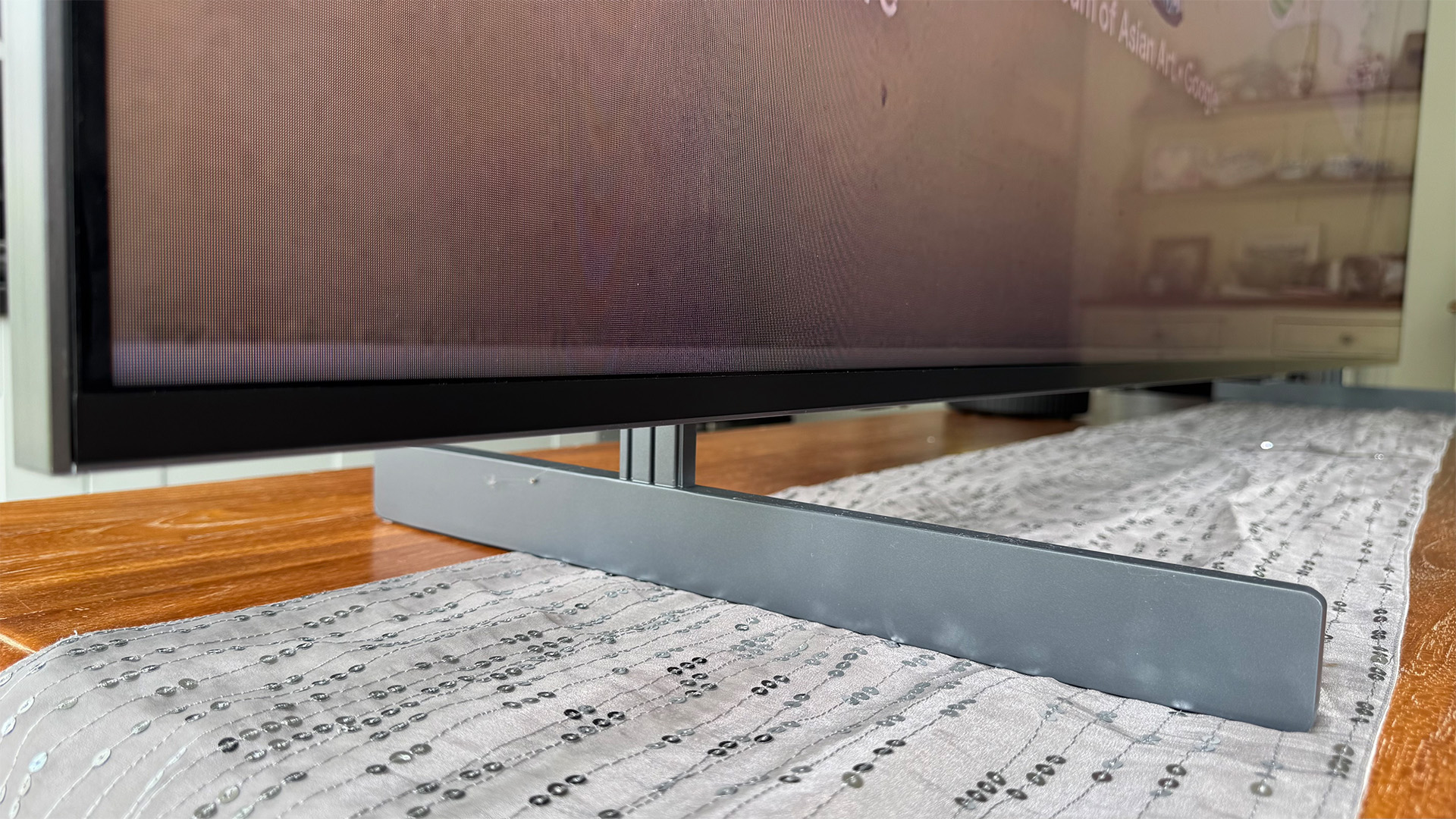 TCL 98C7K 98-inch TV on dining table runner close up on feet and bottom edge of screen